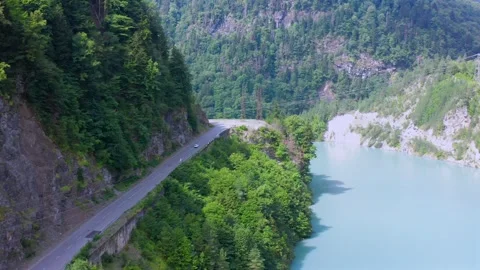 Drone flies forward above Enguri Reservoir road as it curves between forested Vídeo Stock 343543252
