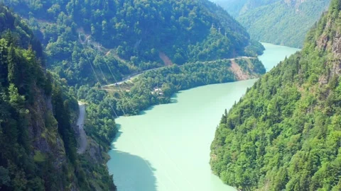 Drone flies forward above Enguri Reservoir through forested mountain terrain Vídeo Stock 343543476
