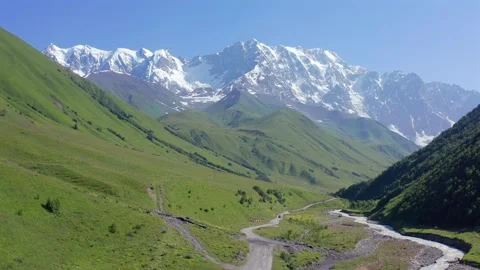 Drone flies forward above Shkhara valley along a remote alpine road near Vídeo Stock 344143530