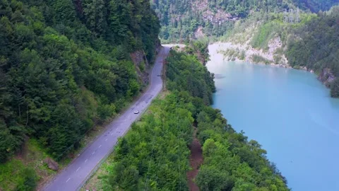 Drone flies forward along Enguri Reservoir road beside turquoise water and steep Vídeo Stock 343543217