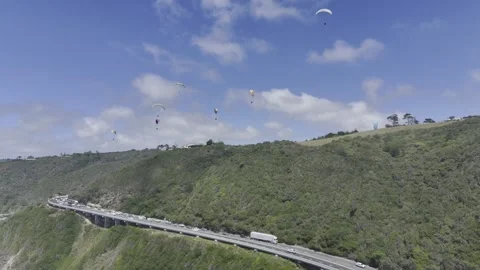Drone flies forward as camera pans up to paragliders over coastal highway Stock Footage 326765172