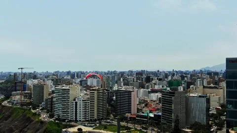 Drone flies forward toward a red paraglider soaring over the Miraflores skyline Vidéo 347834385