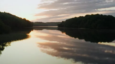 Drone flies low over lake water surface, island backlit with morning sunlight Stock Footage 243228384