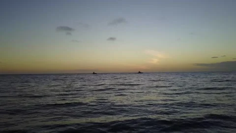 Drone flies low over ocean with boats in distance during sunset 스톡 동영상 244822817