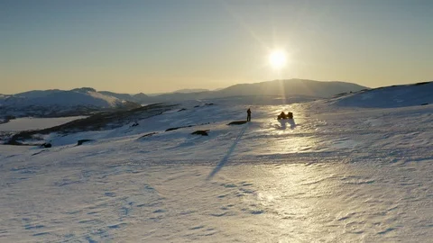 Drone flies low over a standalone person and snowmobile up towards golden Sun Stock Footage 120360901