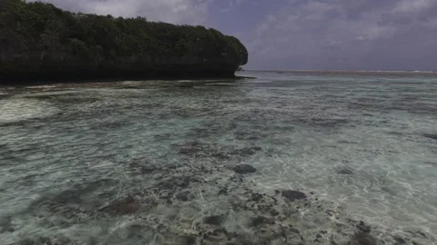 Drone flies low over tide pool and then under cliff on a sunny morning Stock Footage 344057109