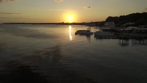 Drone flies low over water toward the sunset on a clear day as speedboat passes Stock Footage 307128079
