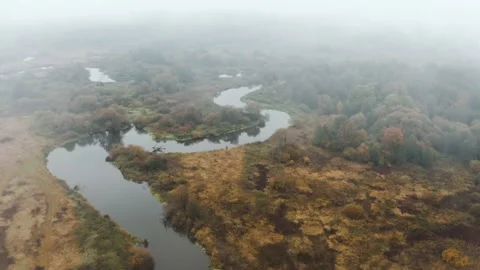 Drone flies in low rain clouds moving over winding river and fall colors trees Stock Footage 141769612