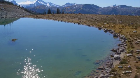 Drone Flies over Alpine Lake Panning up to Mountain Ski Resort in Summer Stock Footage 82635610