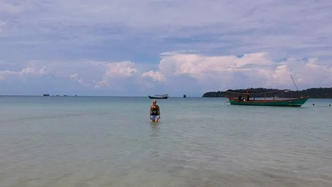 Drone flies over a blonde girl standing in the sea with clothes Stock Footage 111394953