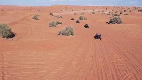 A drone flies over a caravan of buggies driving through the desert sand Stock Footage 251001562