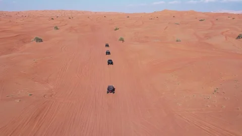 A drone flies over a caravan of buggies driving through the desert sand Stock Footage 255285727