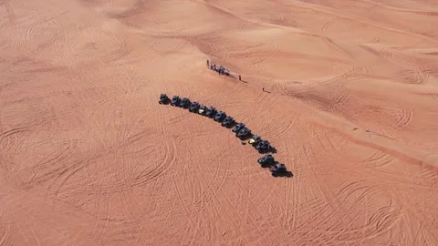 A drone flies over a caravan of buggies standing on a desert sand dune. Stock Footage 255286723