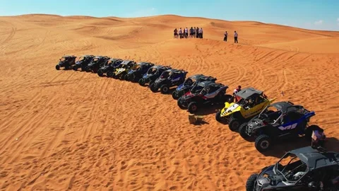 A drone flies over a caravan of buggies standing on a desert sand dune. Stock Footage 256202577