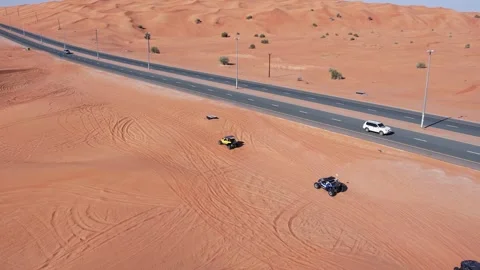 A drone flies over a caravan of buggies driving through the desert sand Stock Footage 340459526