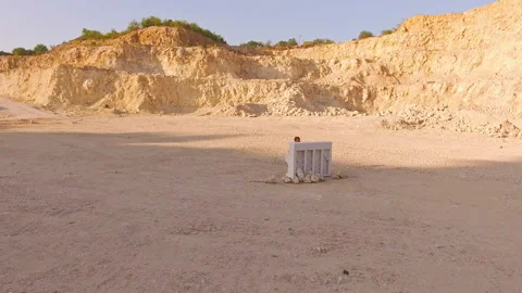 Drone flies over a deep foundation pit in which a man plays the piano. Aerial Stock Footage 94257903