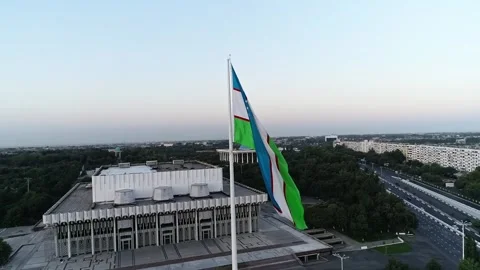 A drone flies over a giant flag in the middle of a city. Sunset sky Stock Footage 334657697