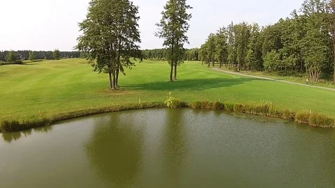 A drone flies over a green golf course with lake Stock Footage 79780443