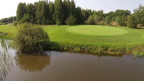 A drone flies over a green golf course with lake Stock Footage 80407248