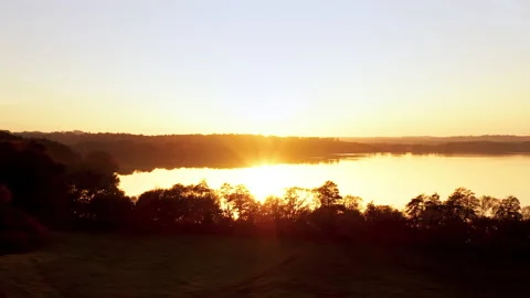 A drone flies over a lake during a sunrise. The reflection of the sun is in the Stock Footage 239103552
