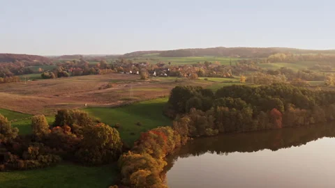 A drone flies over a lake with a view of a street and houses. Trees are Stock Footage 239101389