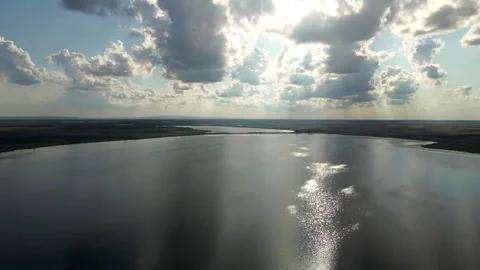 Drone flies over large shiny lake under clouds in sunny day in plain countryside Stock Footage 263321162