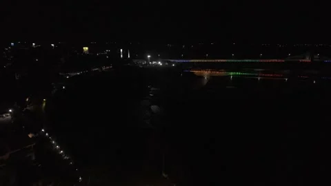 Drone flies over low tide bay at night toward colorfully lit up bridge Video stock 342251246