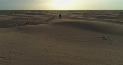 A drone flies over a man in Arab clothes walking on the sand dunes of the desert Stock Footage 277873040