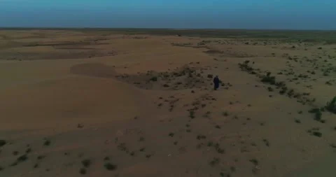 A drone flies over a man in Arab clothes walking on the sand dunes of the desert Stock Footage 308011857