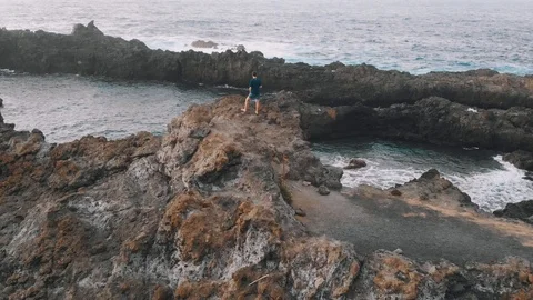 Drone flies over a man who stands at the edge of a volcanic rock. Tenerife Stock Footage 112095988