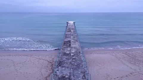 A drone flies over an old pier that extends into the calm sea on a tranquil Video stock 254768245