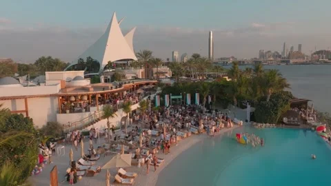 A drone flies over an outdoor pool with a club by the sea, Dubai. People Stock Footage 255703104