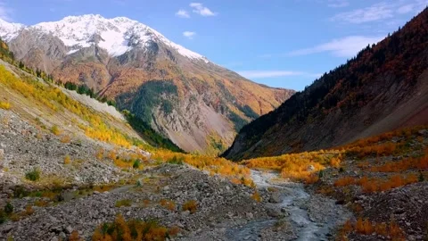 Drone flies over river between mountains in autumn, in distance Chalaadi Glacier 動画素材 164610325