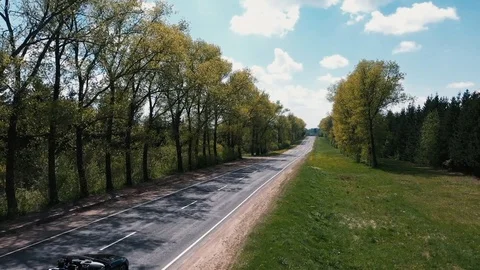 The drone flies over the road between the trees and watching the cars Vidéo 107927061