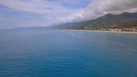 Drone flies over sea surface waves reaching shore, village and mountains Stock Footage 111952019