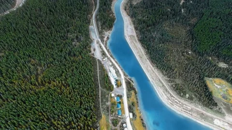 Drone flies over small buildings and trails on the shore of a forest river Video stock 137513133