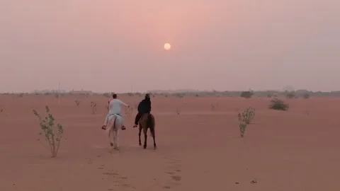 A drone flies over two horsemen riding on desert sand among green bushes Stock Footage 255570573