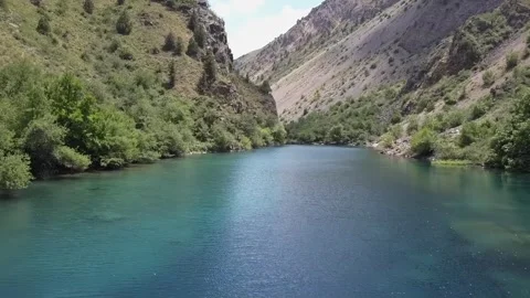A drone flies over the water of a mountain lake in a gorge. Cloudy summer day Stock Footage 309325672