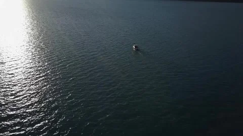 A drone flies over the water of a mountain lake during sunset. A boat floats on Stock Footage 334607831