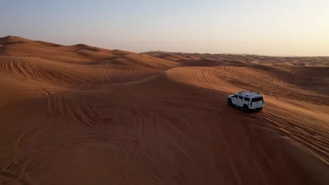 A drone flies over a white SUV driving through the sand dunes of the desert Vídeo Stock 247729660