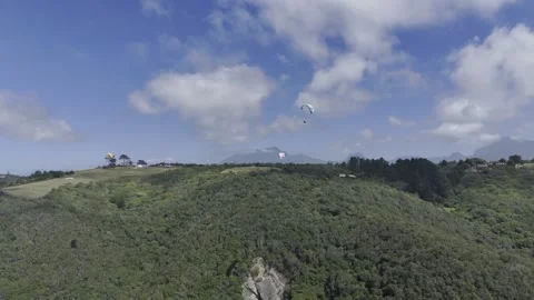 Drone flies right as camera pans left following paragliders over forested hill Stock Footage 326702456