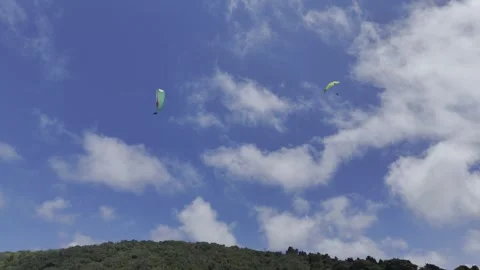 Drone flies to the right looking up at paragliders on a sunny day Stock Footage 326765746