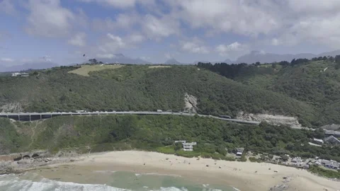 Drone flies to the right with view of beach, coastal highway and forested hill Stock Footage 326749651