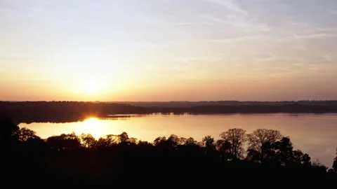 A drone flies sideways next to a lake. The sun is low and reflected in the Stock Footage 239105217