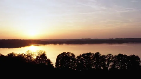 A drone flies sideways next to a lake. The sun is low and reflected in the Stock Footage 239105461