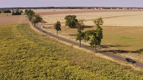 A drone flies sideways overlooking a busy country road during summer in Stock Footage 239112177