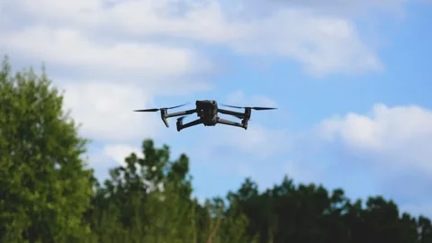 The drone flies in the sky against the background of clouds. Green trees are Stock Footage 312918335