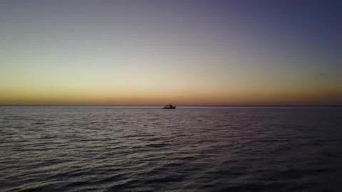 Drone flies slowly over the ocean during sunset as a boat passes in the distance 스톡 동영상 244822828