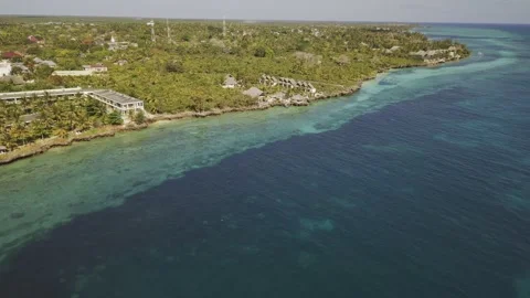 Drone flies from turquoise blue water toward seaside resort nestled in Stock-Footage 346470970