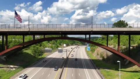 Drone flies under bridge over interstate traffic toward giant American flag Stock Footage 340579055